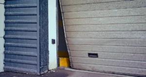 Commercial overhead garage door off track and leaning at an industrial facility entrance